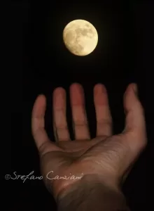 Mano verso la Luna Una mano che sembra toccare una luna piena nel cielo notturno