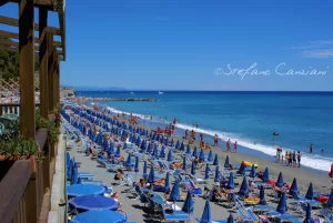 Spiaggia affollata in una giornata di sole Spiaggia affollata con lettini e ombrelloni colorati di fronte a un mare blu limpido