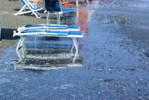 Lettini da spiaggia in riva al mare Lettini da spiaggia bianchi blu riflessi su acqua stagnante con detriti