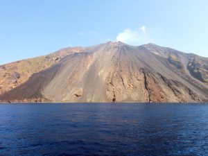 Vulcano attivo in vista dal mare Vulcano attivo con ripida costa di lava che si erge sopra il mare cristallino
