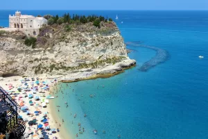 Spiaggia affollata con sdraio e ombrelloni vicino a una scogliera e mare turchese in Calabria