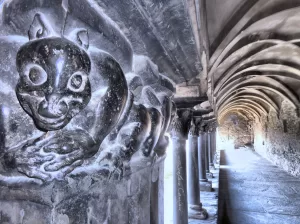 Scultura misteriosa nel chiostro Scultura di un volto misterioso in chiostro con colonne antiche e illuminazione naturale