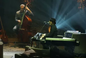 Luciano Ligabue – Concerto di Musica dal Vivo Luciano Ligabue - Un musicista al pianoforte con un bassista sullo sfondo, in un'atmosfera di concerto dal vivo