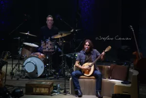 Luciano Ligabue – Concerto dal Vivo con Mandolino Luciano Ligabue - Musician suona un mandolino sul palco con batterista sullo sfondo in un concerto dal vivo