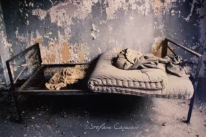 Letto Abbandonato in un Ambiente Deteriorato Un letto abbandonato con un materasso sformato e coperte disordinate in un ambiente deteriorato