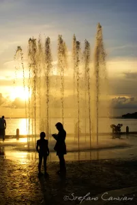Il riflesso d’oro Silhouette di adulti e bambini davanti a un'installazione di fontane al tramonto