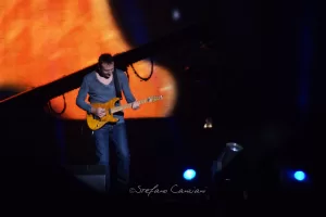 Luciano Ligabue – Chitarrista in azione Luciano Ligabue - Musicista su palcoscenico che suona chitarra elettrica con sfondo luminoso