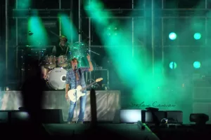 Luciano Ligabue – Concerto dal Vivo Luciano Ligabue - Concerto di una band con luci verdi e un chitarrista che si esibisce sul palco