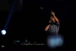 Luciano Ligabue – Concerto di un artista in azione Luciano Ligabue - Artista in concerto che canta e interagisce con il pubblico sullo sfondo di luci sfocate