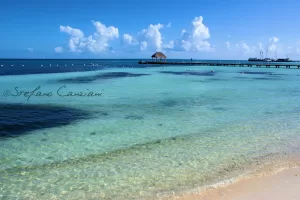 Spiaggia tropicale con acqua cristallina e pontile, cielo blu e nuvole bianche