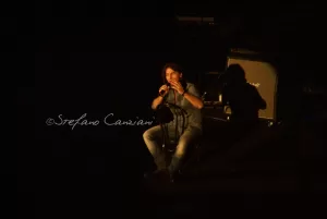 Luciano Ligabue - Esibizione di un cantante sul palco Luciano Ligabue - Cantante che si esibisce sul palco con luci soffuse e ombre sullo sfondo