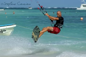Kitesurf in azione Un atleta di kitesurf mentre salta sopra le onde in una spiaggia soleggiata
