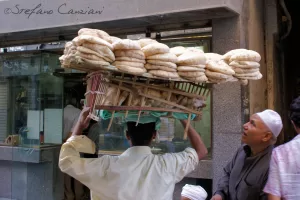 Tradizione in equilibrio Uomo che trasporta un carico di pane su una spalla in un mercato affollato
