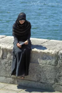 Il tempo si ferma dove la pietra incontra il pensiero Donna con hijab seduta su una pietra vicino all'acqua mentre legge