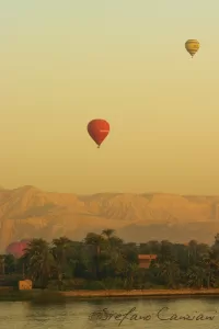 Due mongolfiere sorvolano un paesaggio desertico al tramonto, con montagne sullo sfondo