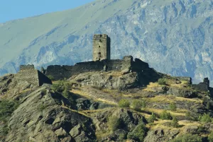 Ruderi di un castello su una collina con montagne sullo sfondo