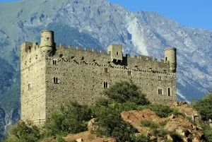 Castello medievale in pietra situato su una collina con montagne sullo sfondo
