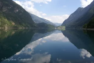 Lago tranquillo circondato da montagne verdi e cielo azzurro, riflessi perfetti sull'acqua