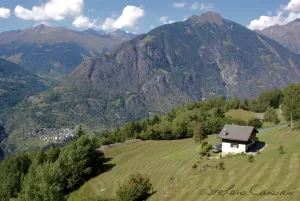Panorama montano con casa rustica e prati verdi in Valtellina