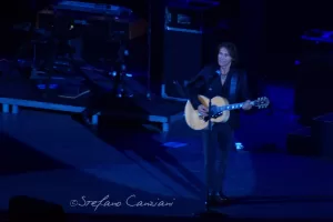 Luciano Ligabue - Concerto di un Musicista Luciano Ligabue - Musicista su un palco con chitarra, illuminato da luci blu durante un concerto