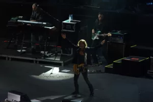 Luciano Ligabue - Performance dal Vivo di un Musicista Luciano Ligabue - Un musicista sul palco con una chitarra, mentre altri musicisti suonano sullo sfondo