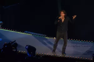 Luciano Ligabue - Performance dal vivo di un cantante Luciano Ligabue - Un cantante in abbigliamento scuro si esibisce su un palco illuminato