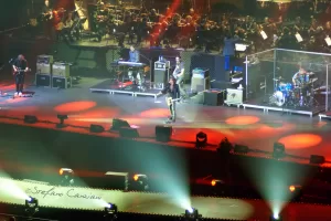 Luciano Ligabue - Concerto dal Vivo Luciano Ligabue - Concerto dal vivo con musicisti su palco illuminato da luci colorate e orchestra sullo sfondo