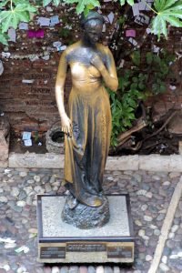 Statua di donna in abito elegante Statua bronzea di una donna in abito elegante, circondata da piante verdi