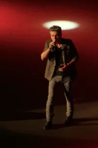 Luciano Ligabue - Cantante in performance Luciano Ligabue - Un uomo canta sul palco, illuminato da un fascio di luce rossa e bianca