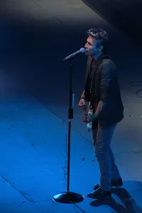 Luciano Ligabue - Performance Musicale Luciano Ligabue - Cantante maschile sul palco con chitarra e microfono, illuminato da luci blu