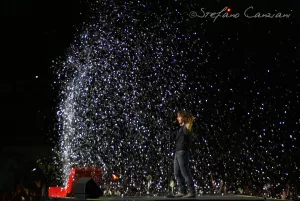 Luciano Ligabue - Concerto con effetti visivi brillanti Luciano Ligabue - Artista sul palco circondato da effetti scintillanti durante un concerto