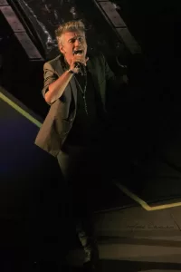 Luciano Ligabue - Esibizione dal Vivo Luciano Ligabue - Cantante che si esibisce su un palco con abito elegante