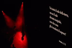 Luciano Ligabue - Messaggio di speranza Luciano Ligabue - Immagine di un palco illuminato da luci rosse con proiezione di un testo biblico