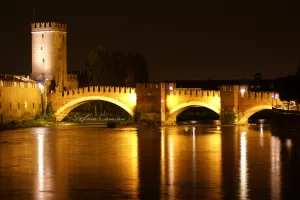 Ponte storico illuminato di notte con torri e refletti sull'acqua