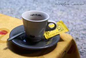 Tazza di caffè e zucchero Tazza di caffè su piattino grigio con zucchero in bustina su tavolo giallo