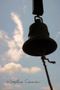 Campana in silhouette contro un cielo azzurro con nuvole bianche