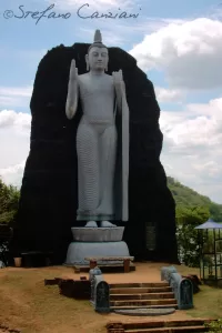 Statua di Buddha eretta su una roccia scura con cielo blu e nuvole