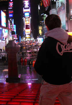 Un giovane in felpa nera guarda verso Times Square illuminata di notte con cartelloni pubblicitari